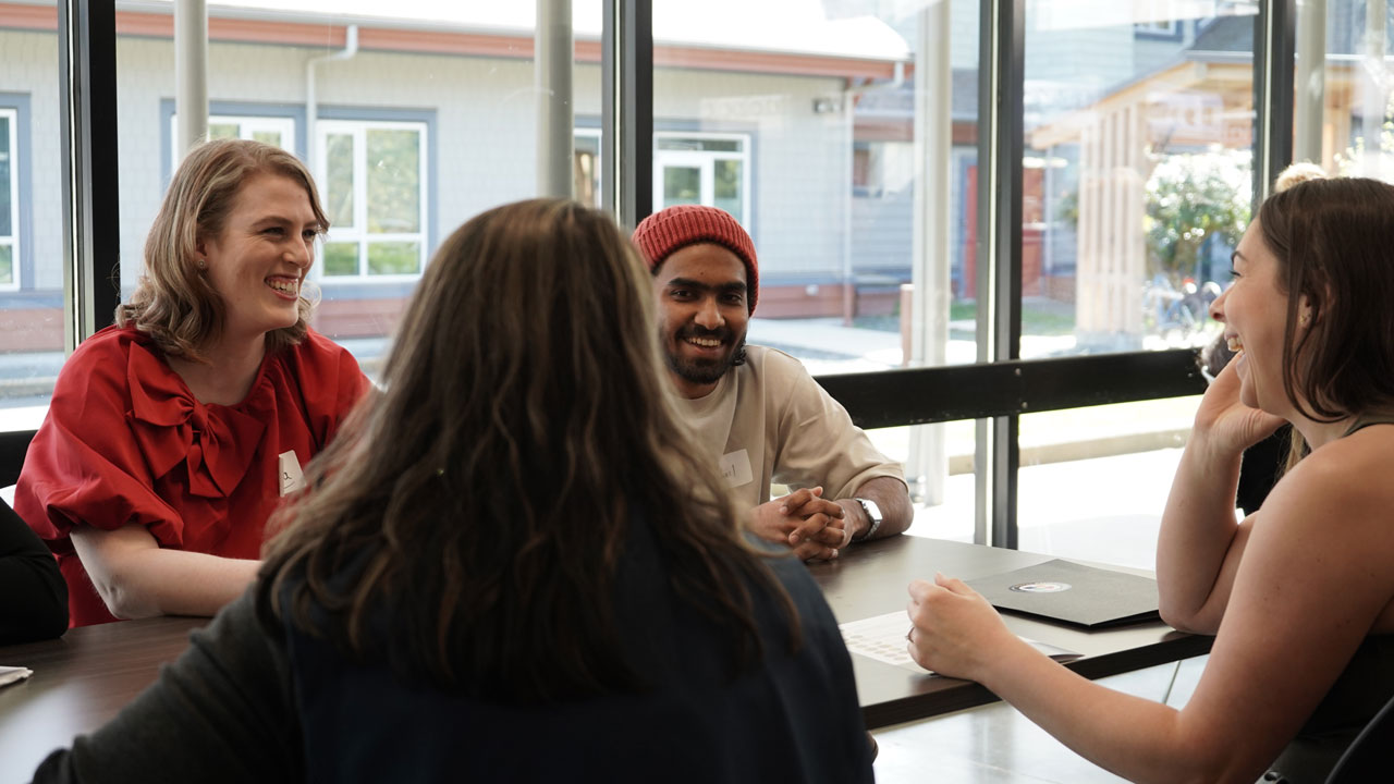Students gathered around a table, smiling in conversation at a Comox Valley student common space.